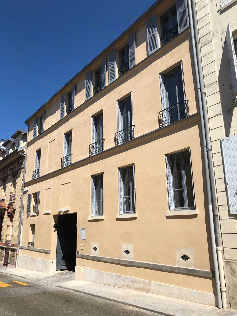 Immeuble d'appartements beige dans une rue ensoleillée.