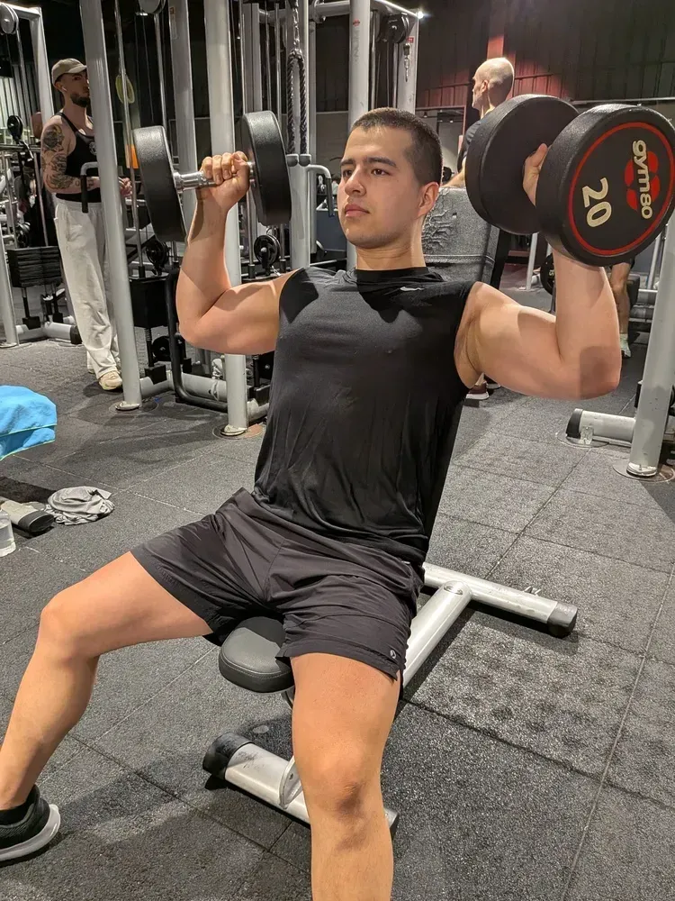 Persona haciendo press de hombros con mancuernas sentado en una máquina en el gimnasio