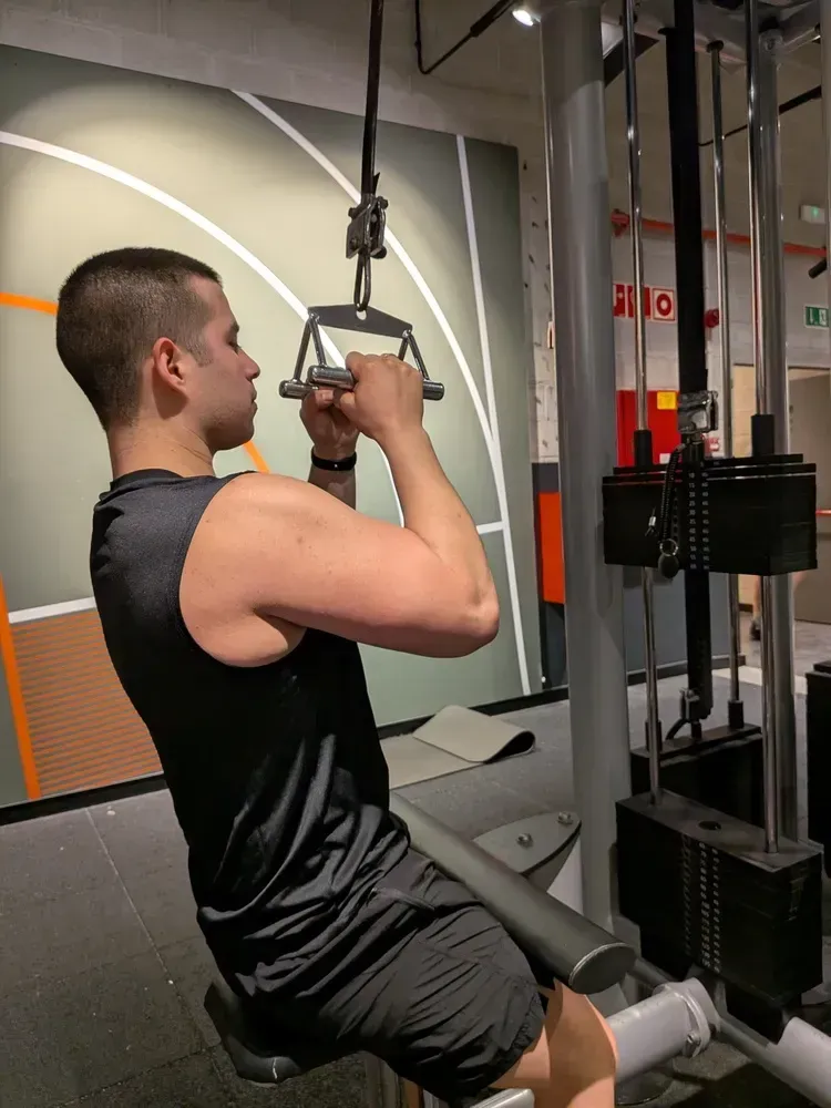 Hombre haciendo un ejercicio de pulldown dorsal en un gimnasio, tirando hacia abajo en una máquina de cable.