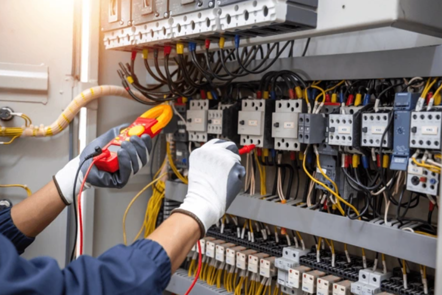 Técnico probando el cableado del panel de control eléctrico con un multímetro y guantes aislantes.