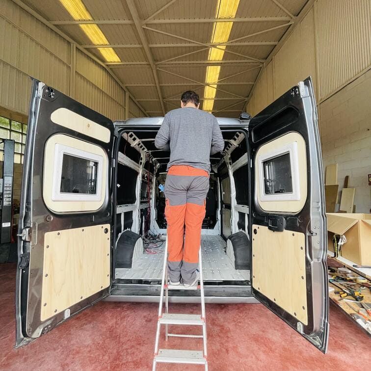 Un hombre parado en una escalera frente a una camioneta con las puertas abiertas.