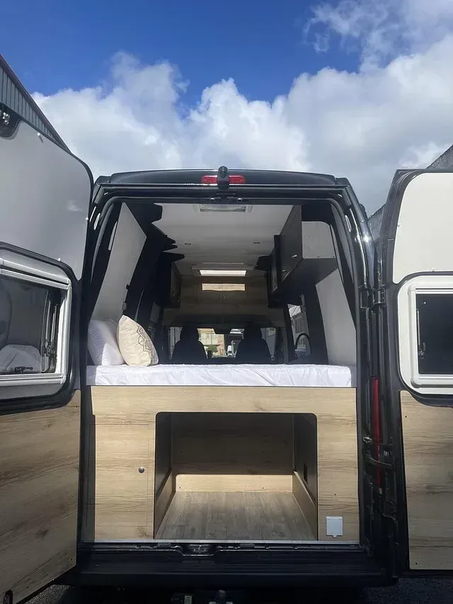 La parte trasera de una camioneta con las puertas abiertas y una cama en la parte trasera.