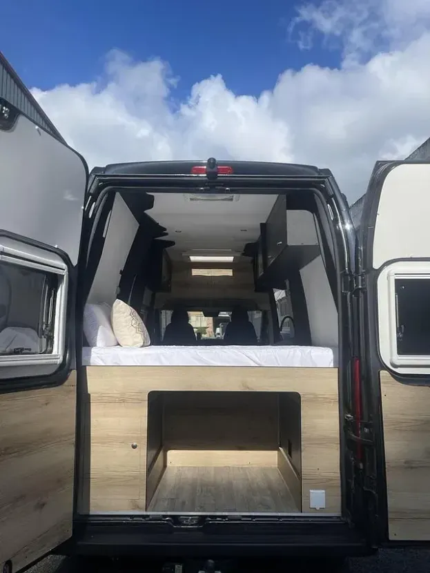 La parte trasera de una camioneta con las puertas abiertas y una cama en la parte trasera.