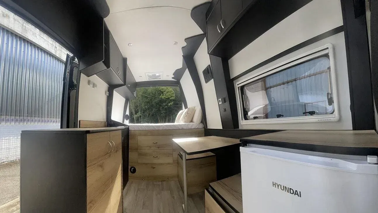 El interior de una furgoneta camper con nevera y cama.