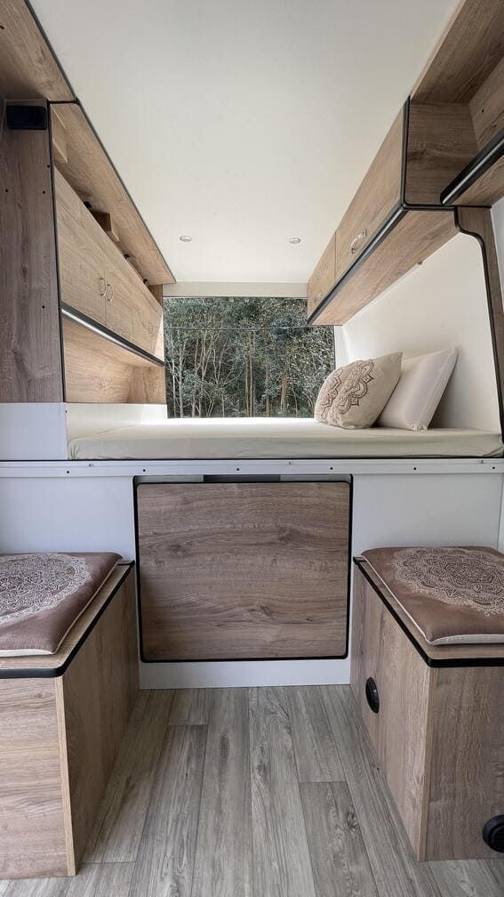 El interior de una furgoneta con muebles de madera y una cama.