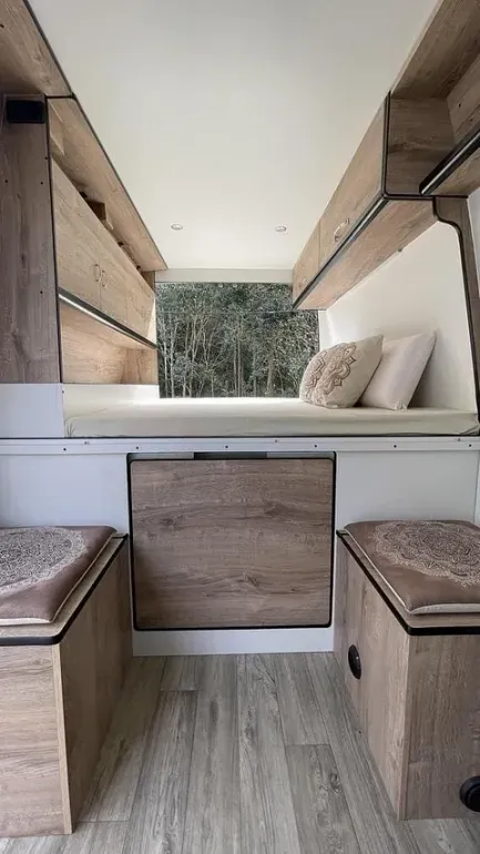 El interior de una camioneta con muebles de madera y una cama.