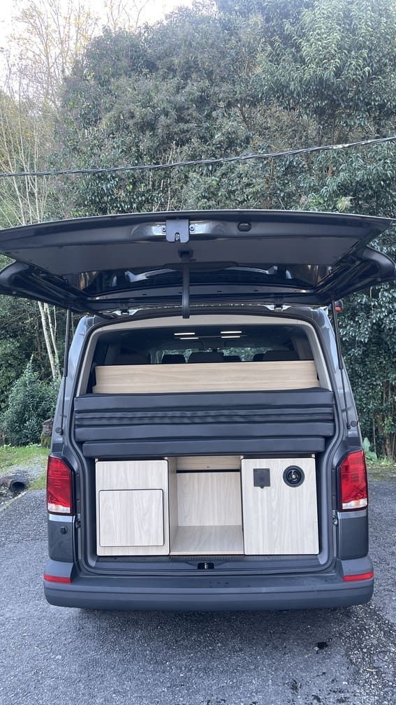 La parte trasera de una camioneta con el maletero abierto está estacionada al costado de la carretera.