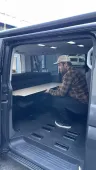 Un hombre está sentado en la parte trasera de una camioneta sosteniendo un trozo de madera.