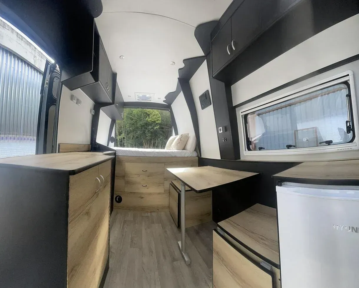 El interior de una furgoneta con armarios de madera y una mesa.