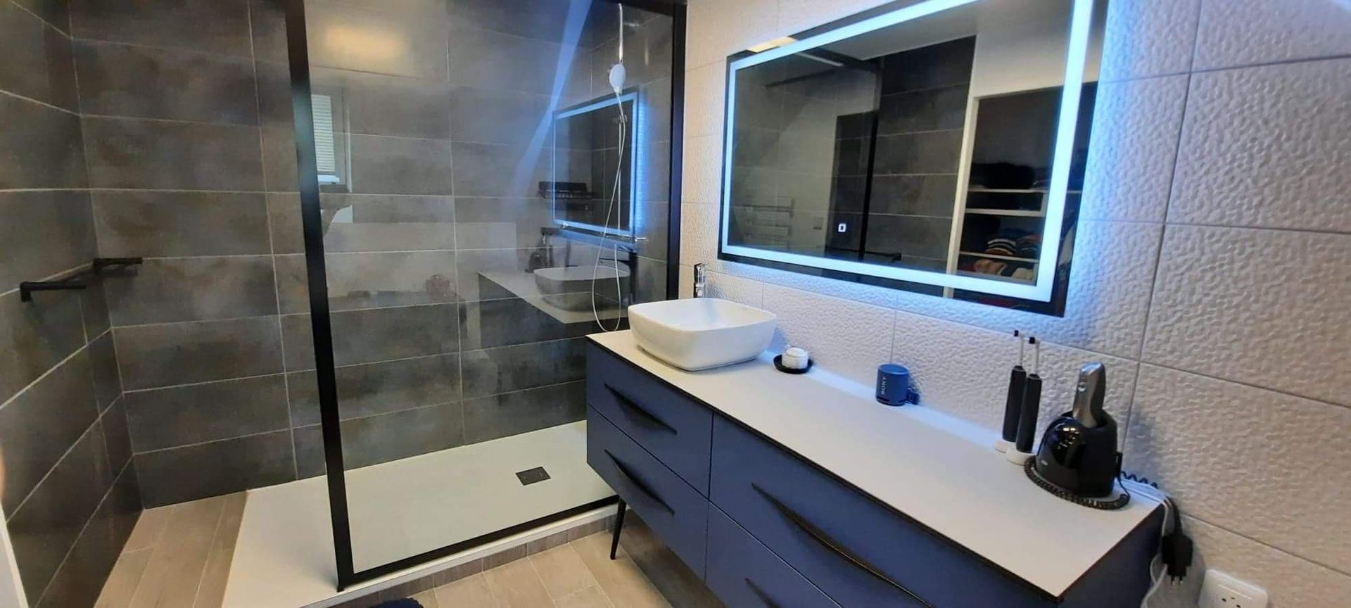 Une salle de bains avec une douche, un lavabo et un miroir avec des led