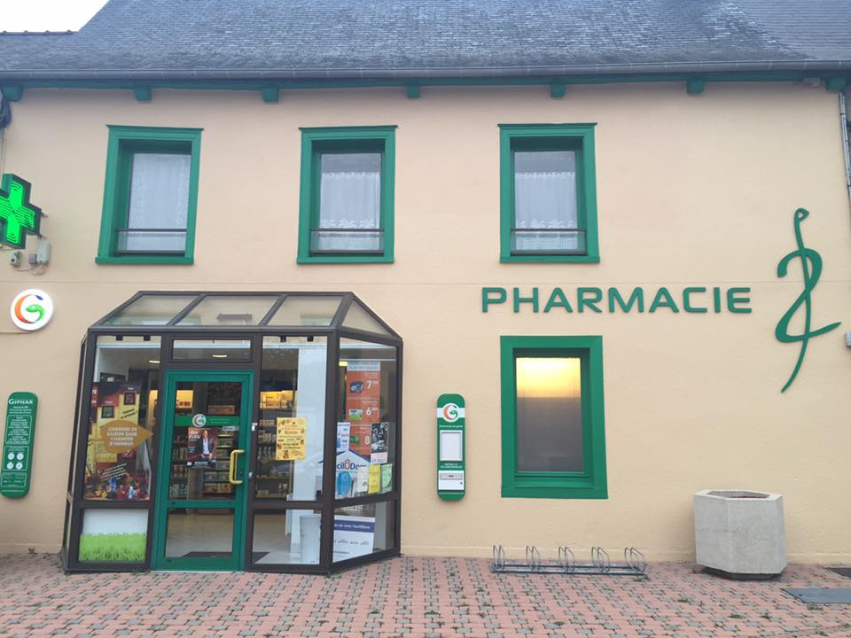 Pharmacie aux accents verts, fenêtres et enseigne, sur une rue pavée de briques.