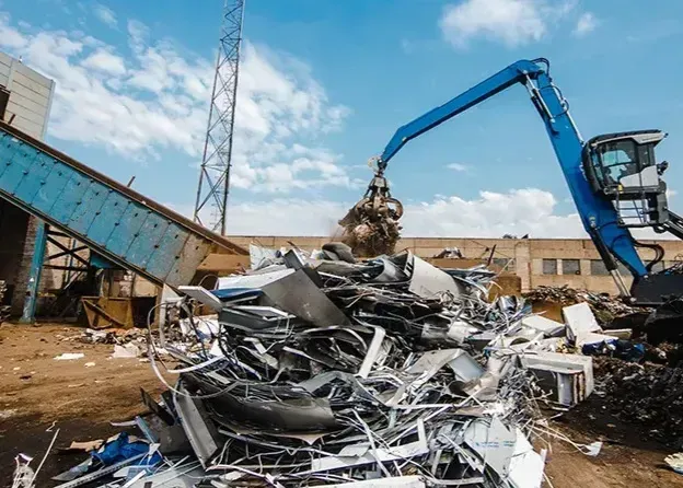 Excavadora amarilla con brazo de garra en una planta de reciclaje, cerca de balas de plástico clasificado.