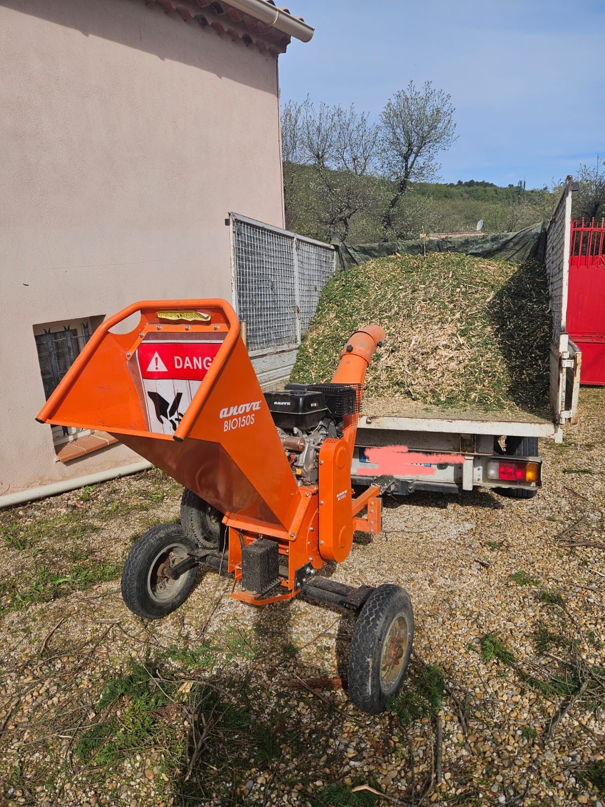 Broyeur de bois orange devant un camion rempli de copeaux de bois, à l'extérieur.
