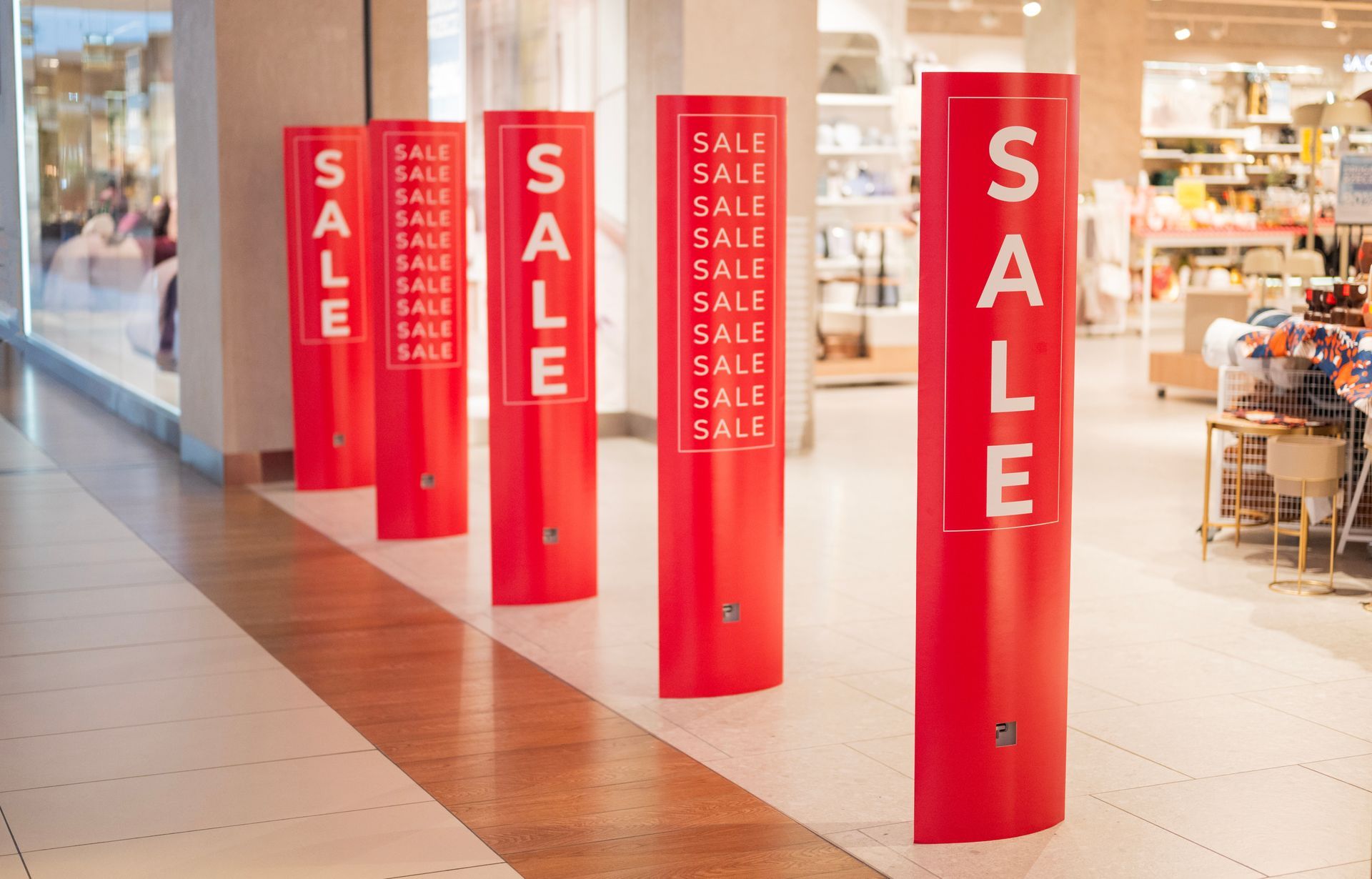 Des panneaux rouges SOLDES sont installés dans une allée de centre commercial, devant les vitrines des magasins.