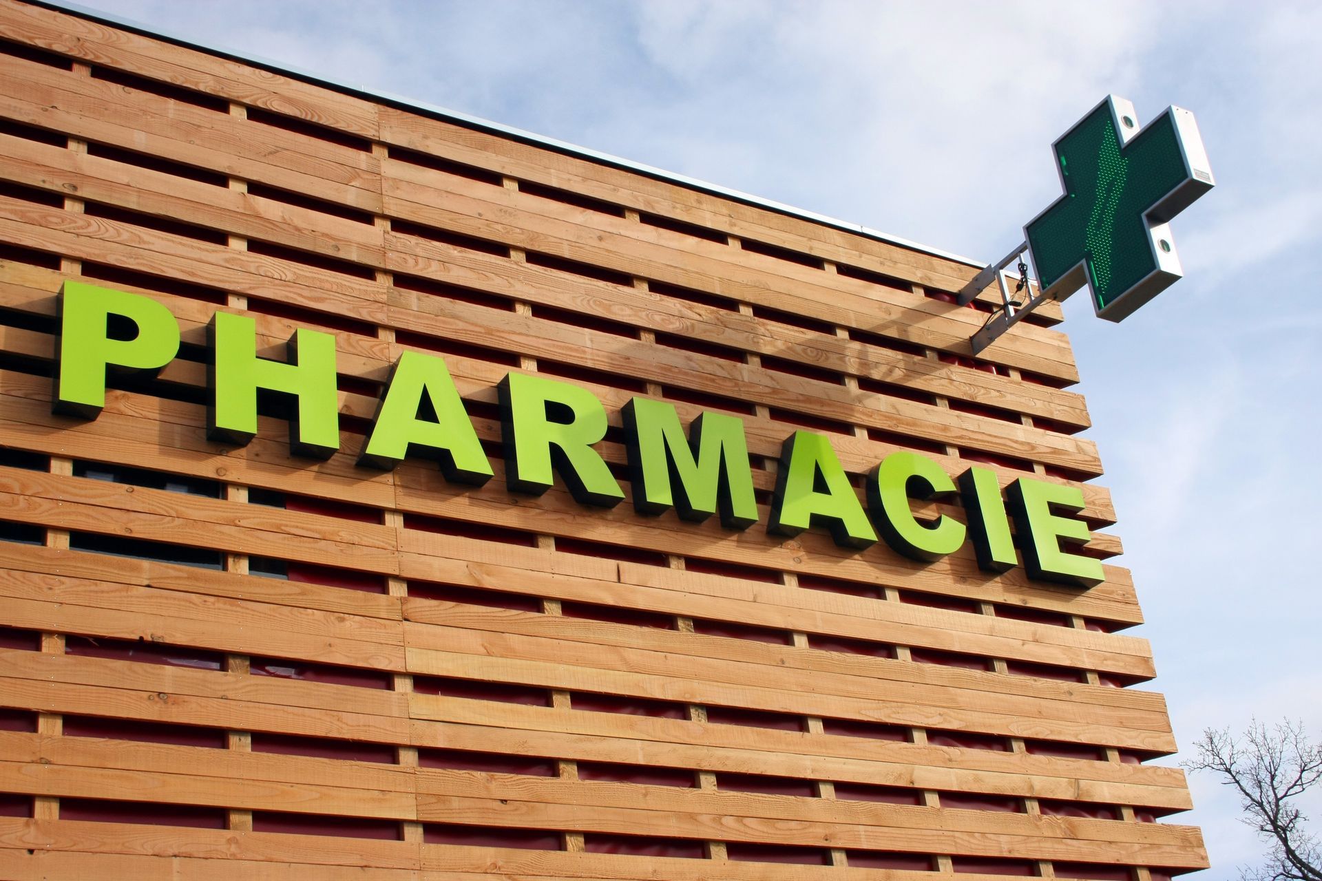 Enseigne verte de pharmacie sur la façade d’un bâtiment en bois, sur fond de ciel bleu
