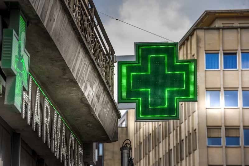 Enseigne lumineuse de pharmacie en forme de croix verte, suspendue entre des immeubles de la ville