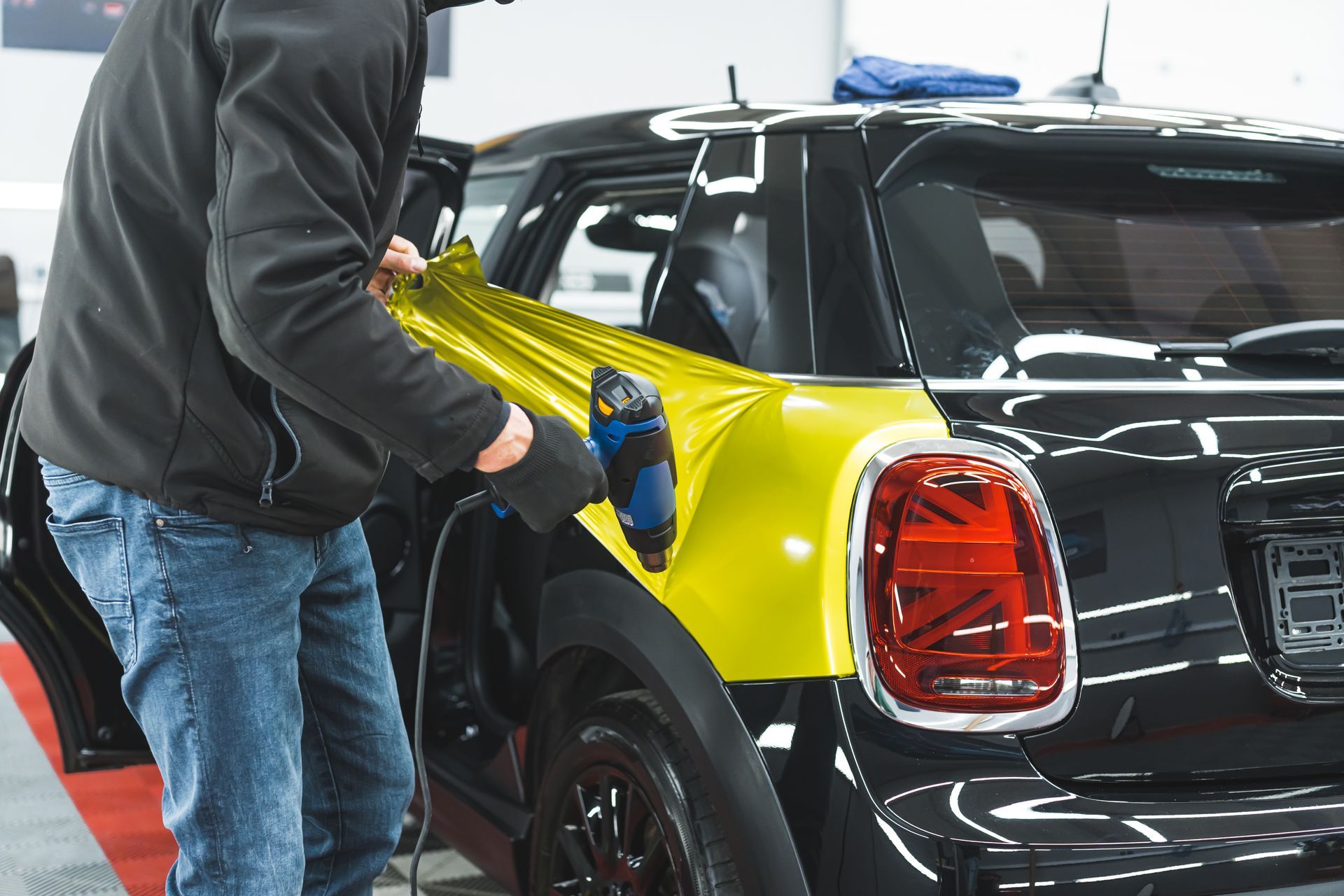 Personne appliquant un film vinyle jaune sur une voiture noire dans un atelier