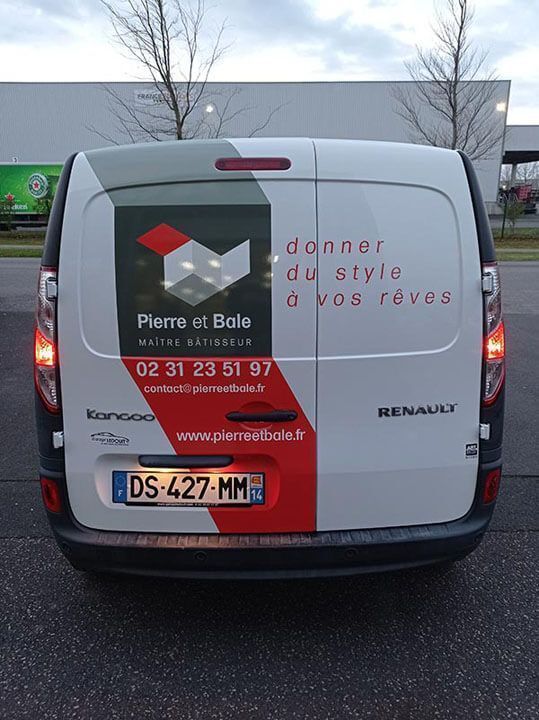Fourgon Renault blanc avec un texte publicitaire rouge, garé dehors sur un sol mouillé.