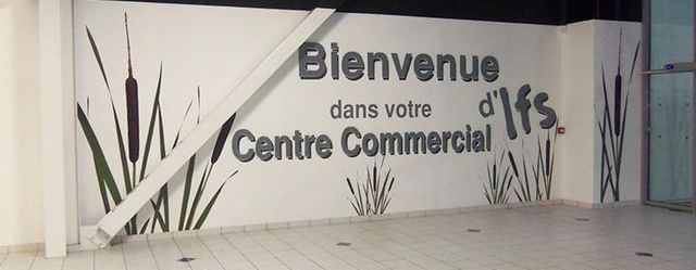 Panneau sur un mur blanc dans un couloir de centre commercial, avec de grands motifs de plantes.