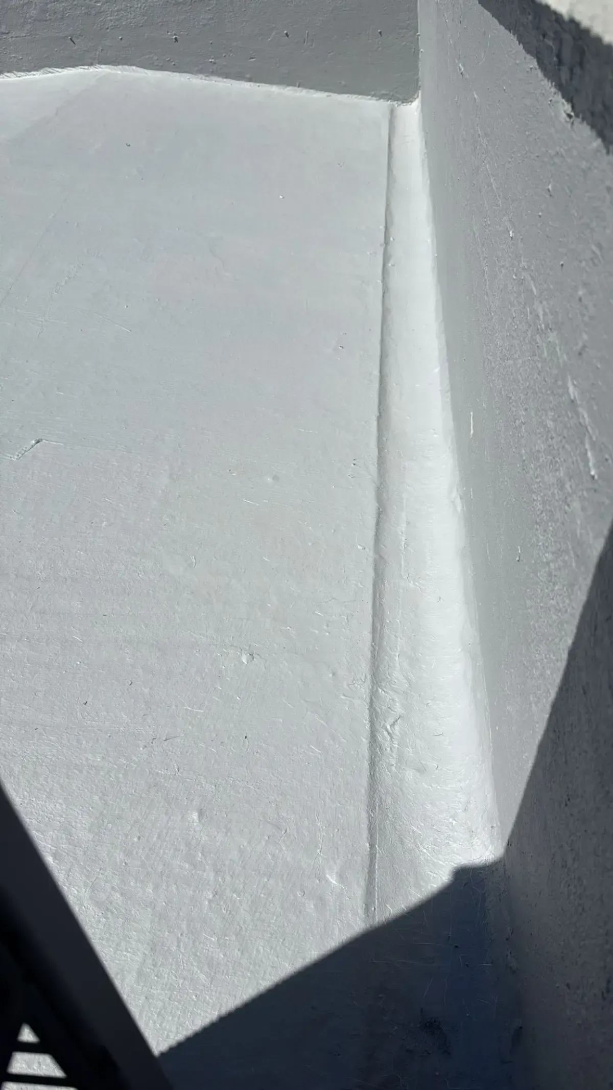 Primer plano de una superficie de techo plana de color gris claro que se une a una pared vertical con una junta lisa