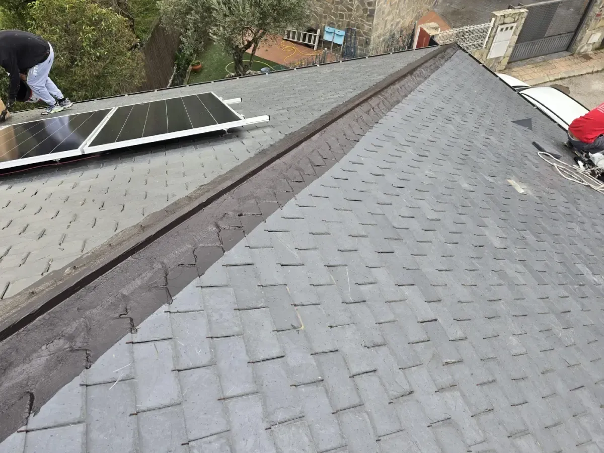 Se están instalando paneles solares en un tejado de tejas de pizarra gris, y se puede ver a un trabajador 
