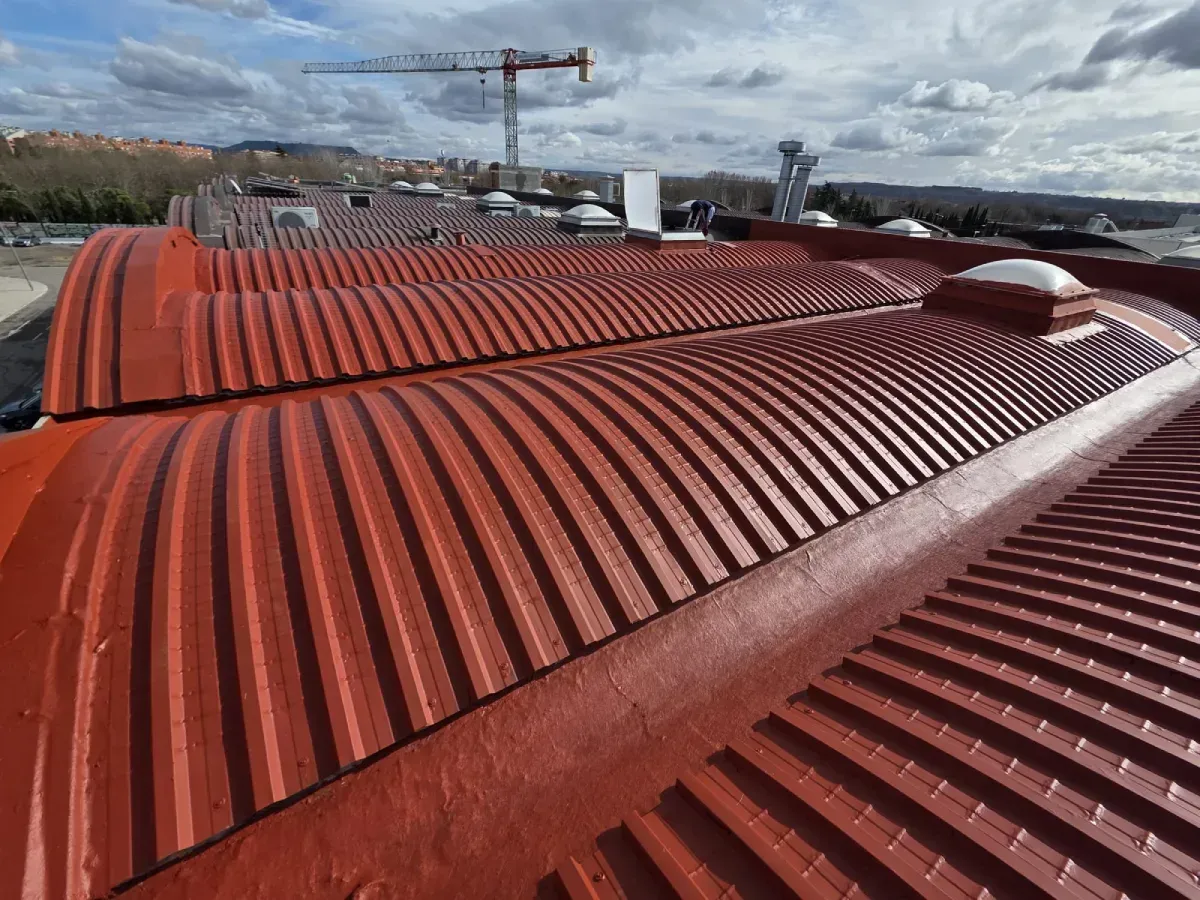 Vista ligeramente elevada de una serie de techos curvos de metal corrugado rojo que forman parte de un almacén