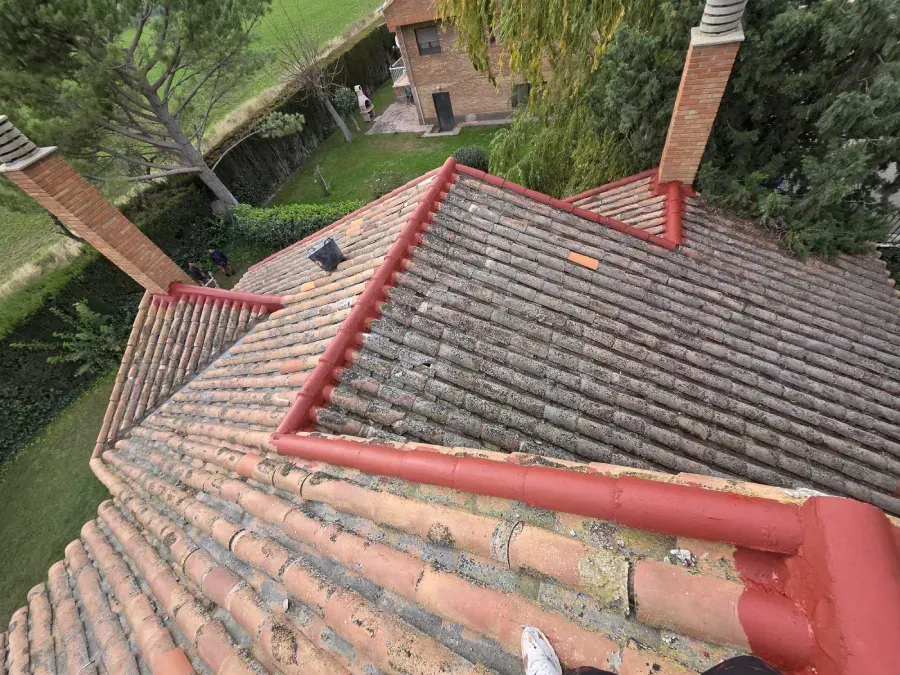 Vista desde un ángulo elevado de un tejado de tejas con tejas de arcilla roja desgastadas y una cumbrera roja
