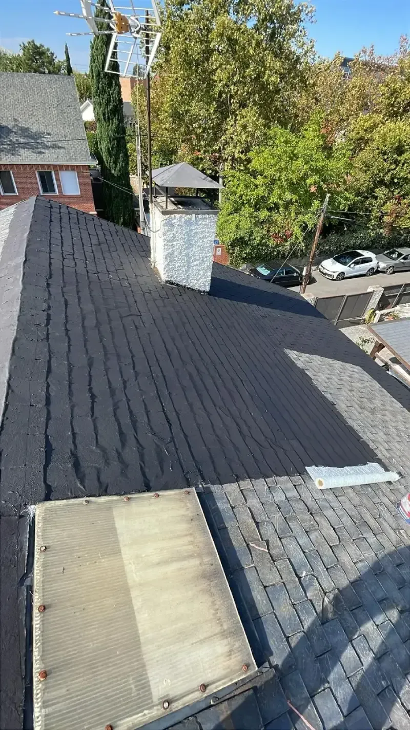 Un tejado parcialmente cubierto con tejas negras nuevas junto a una sección antigua de tejas grises