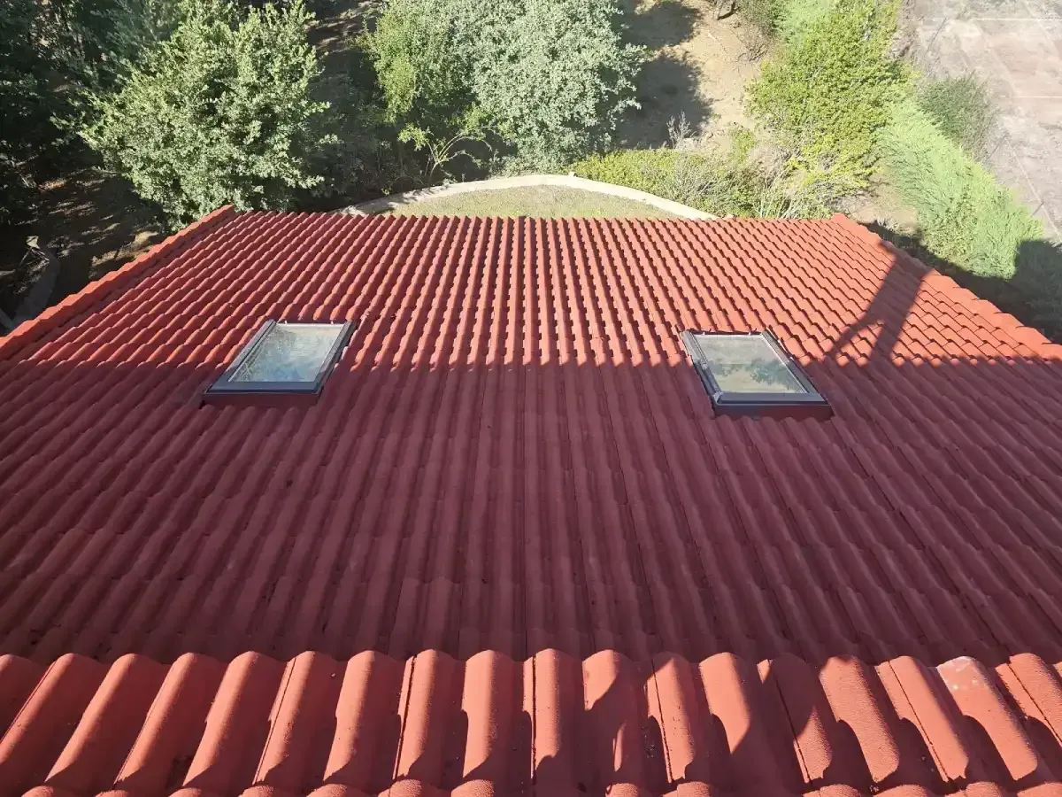Un tejado residencial de tejas rojas con dos claraboyas rectangulares, visto desde un ángulo elevado