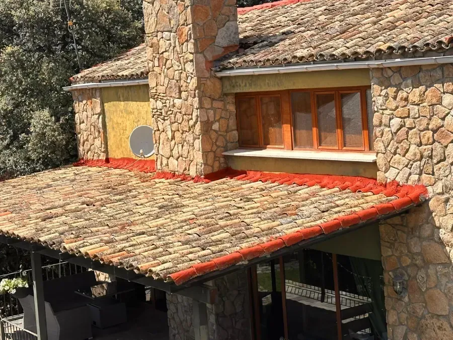 Una casa rústica de piedra con tejado de tejas, una gran chimenea de piedra y un patio cubierto por un tejado