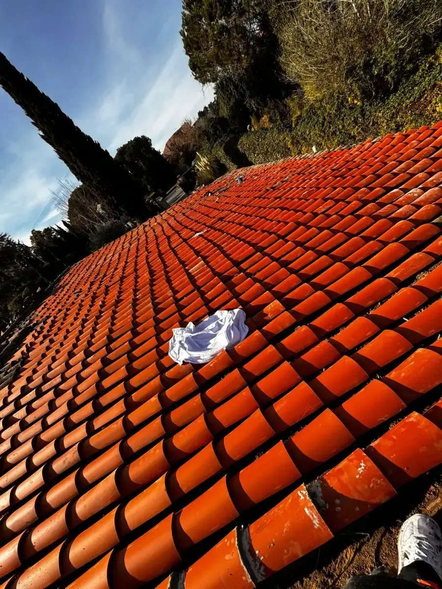 Vista inclinada de un tejado de tejas de color naranja rojizo bajo un cielo azul brillante, con un paño blanco