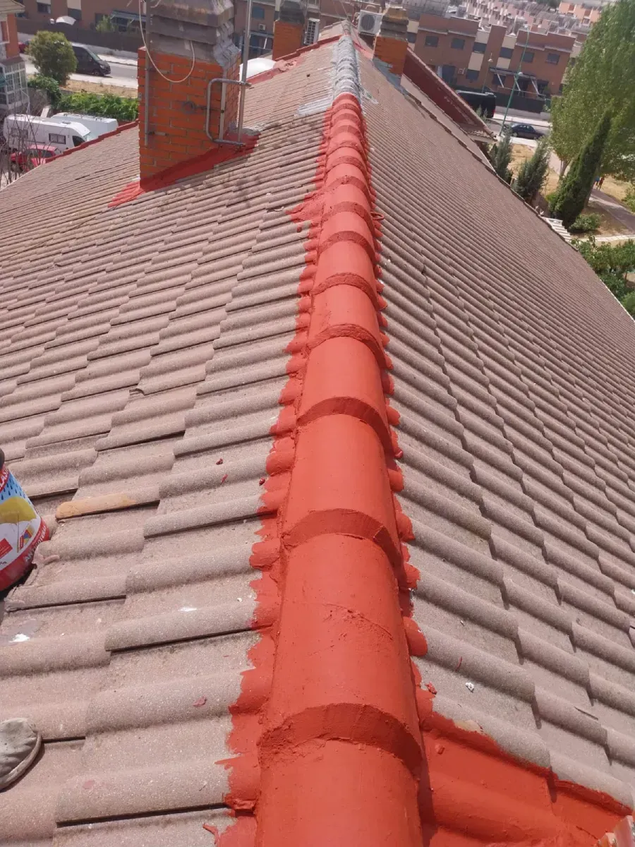 Un tejado inclinado de tejas con una cumbrera recién sellada con mortero rojo brillante y uniforme.