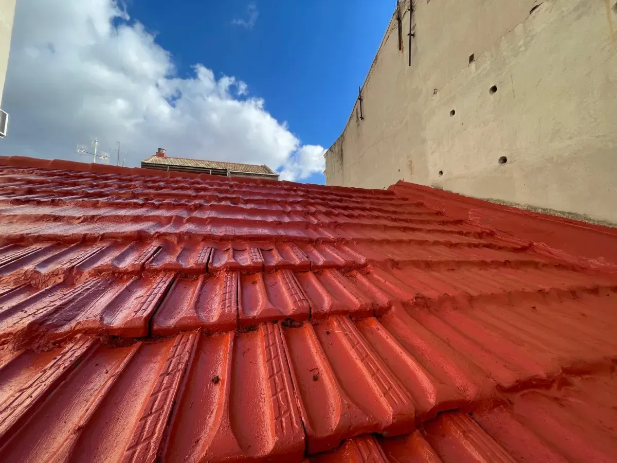 Un tejado de tejas rojas brillantes recién pintado, visto desde un ángulo bajo contra un cielo azul nublado