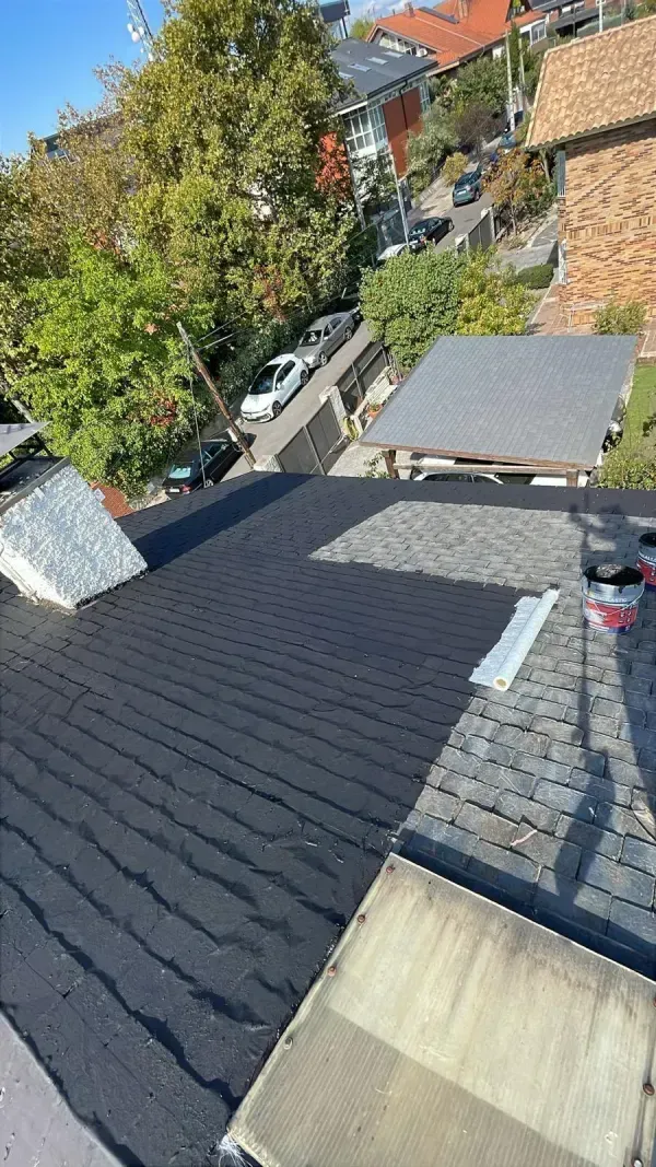 Vista elevada de un tejado residencial que muestra una reparación en curso con un parche de material de cubierta negro nuevo.