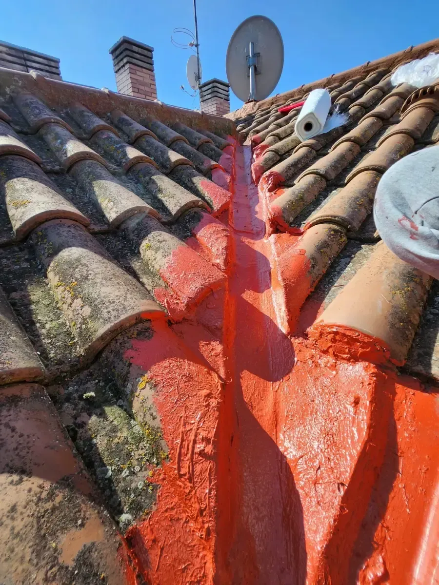 Un canalón entre tejas de terracota, sellado herméticamente con un sellador impermeable de color naranja brillante.