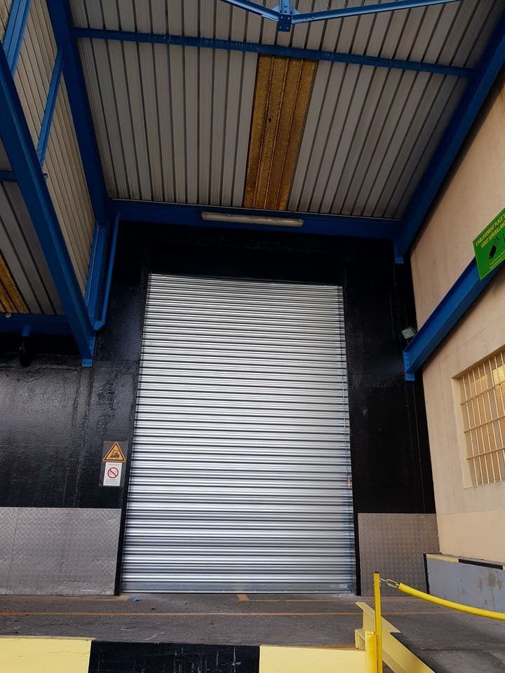 Quai de chargement avec porte métallique ondulée fermée, poutres bleues et barrières de sécurité jaunes.