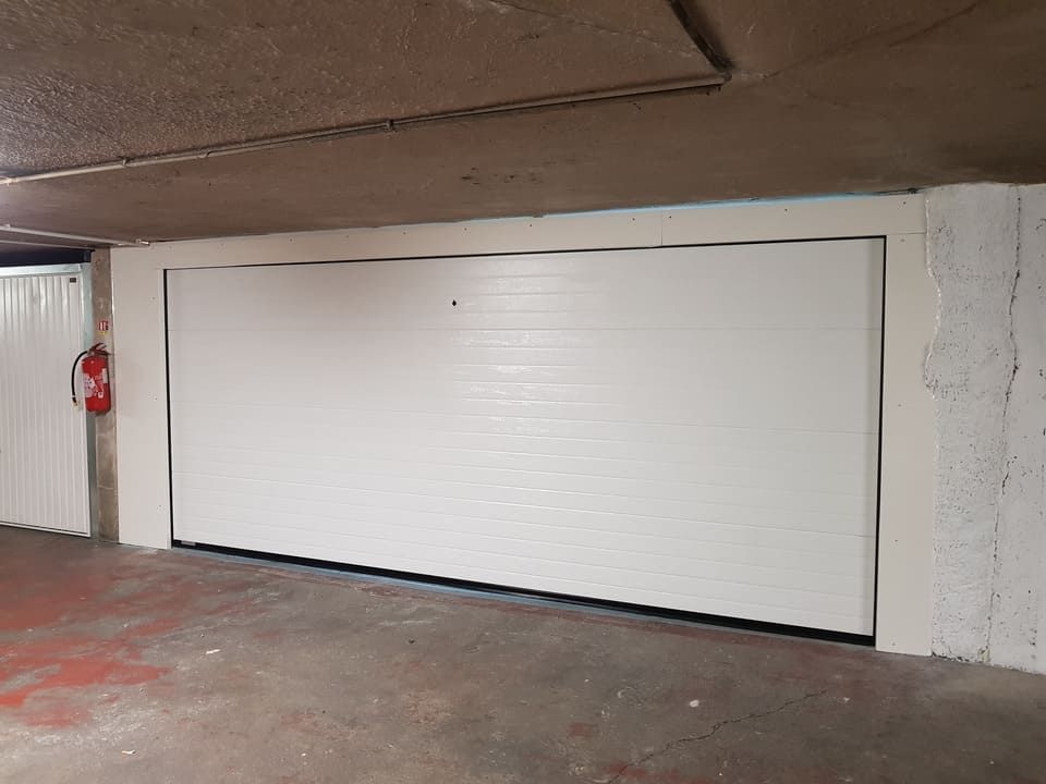 Porte de garage blanche fermée dans un garage en béton. Extincteur sur le mur de gauche.