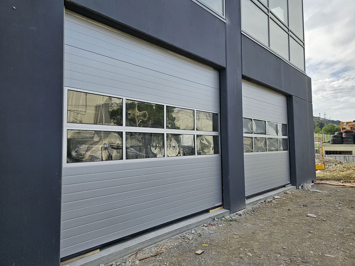 Deux portes de garage grises avec fenêtres sur un bâtiment moderne.