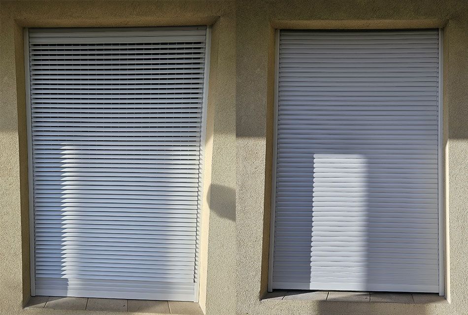 Deux fenêtres avec des volets roulants clairs et fermés dans un bâtiment en stuc.