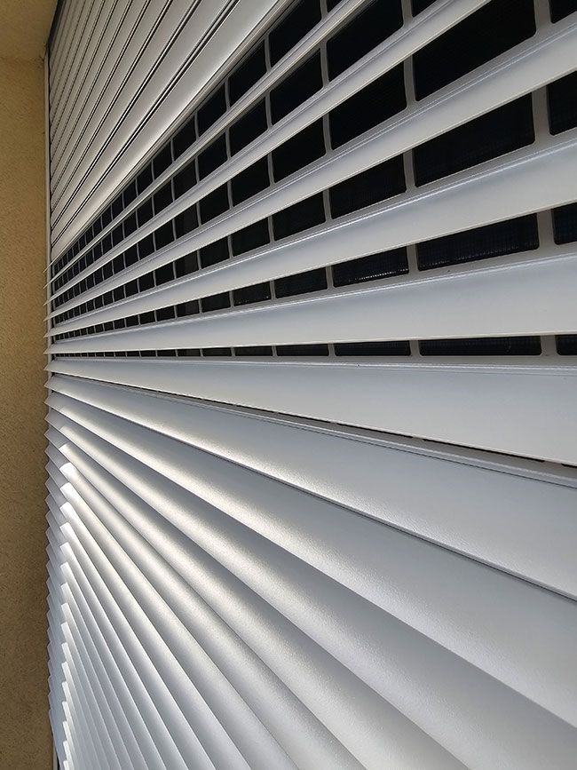 Des stores blancs inclinés recouvrent une fenêtre, laissant entrer un peu de lumière.