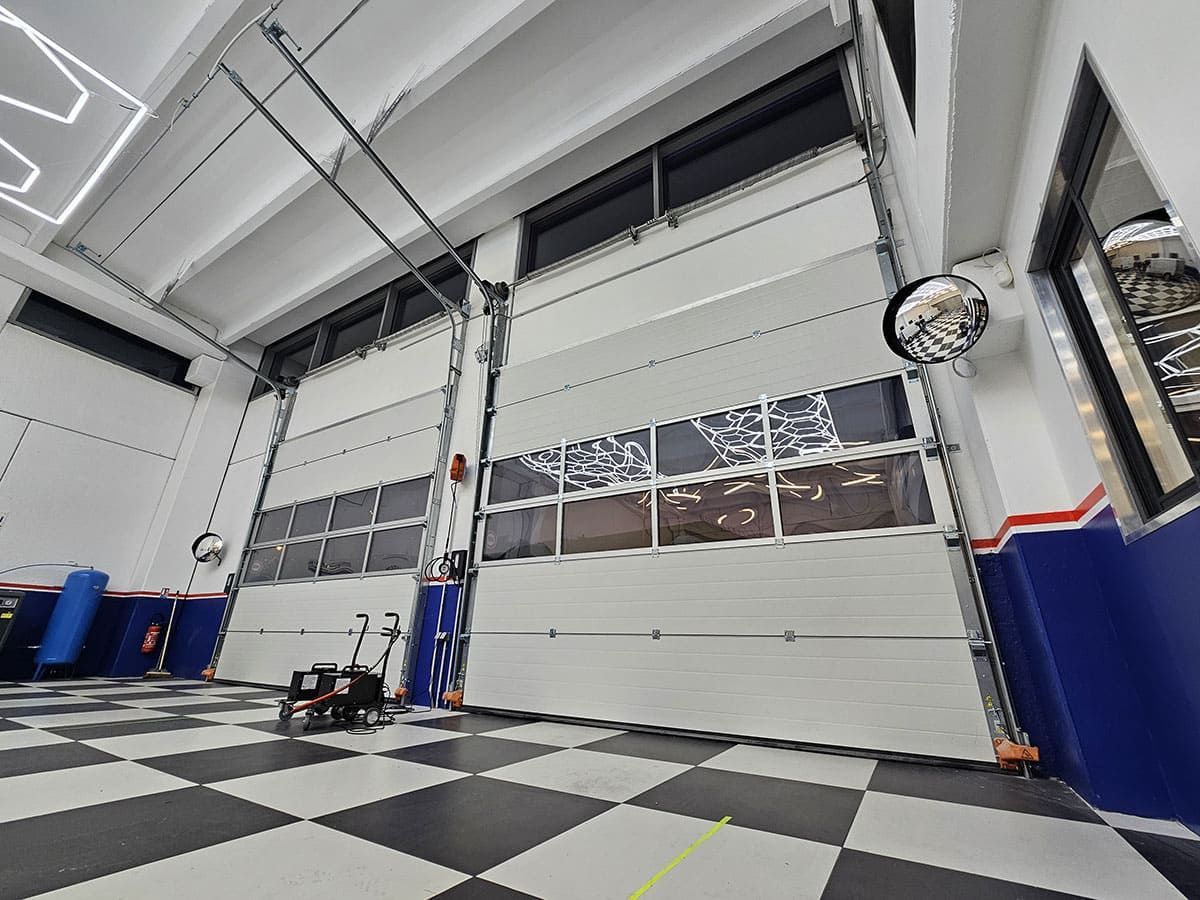 Intérieur du garage avec deux grandes portes blanches, un sol à damier et des fenêtres.