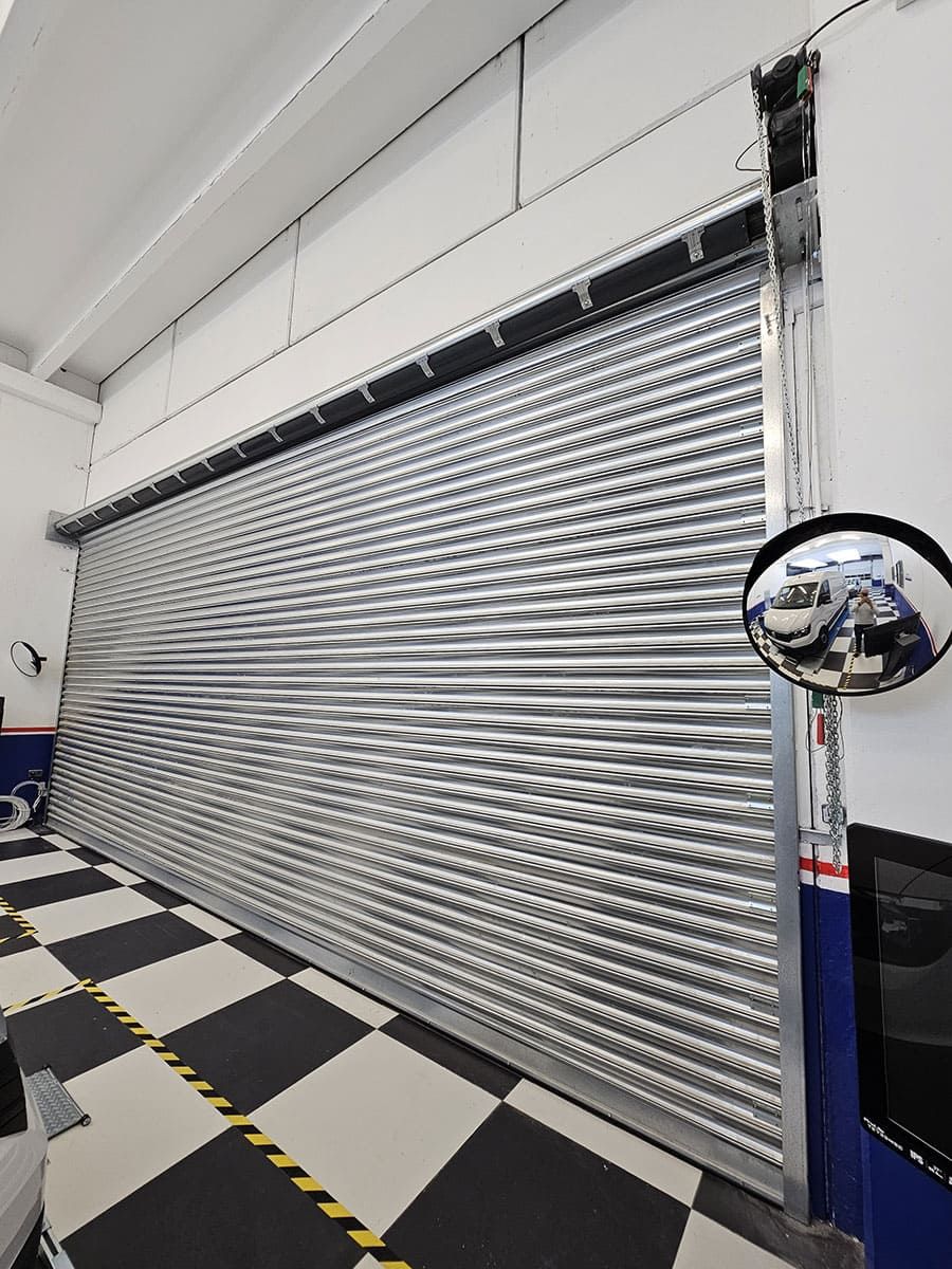 Porte de garage métallique coulissante, fermée, dans un atelier au sol en damier.