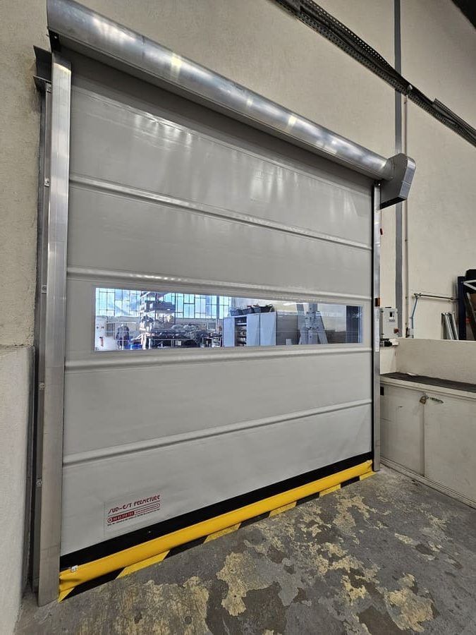 Porte sectionnelle industrielle grise et blanche avec fenêtre et bandes de sécurité.