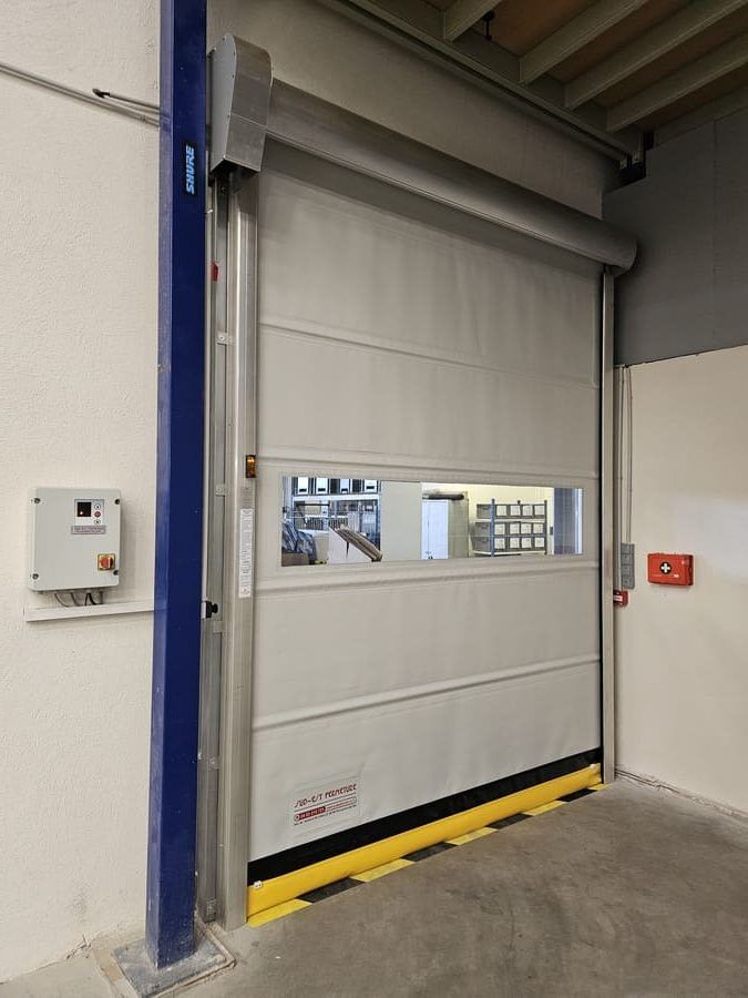 Porte sectionnelle industrielle blanche et grise avec fenêtre et dispositifs de sécurité, pour intérieur.