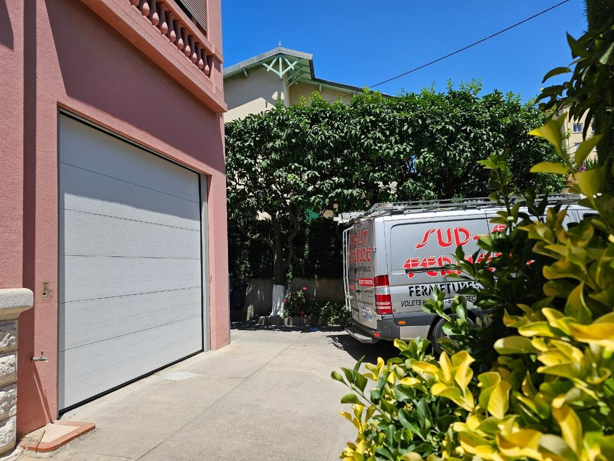 Porte de garage grise à côté d'un bâtiment rose ; camionnette garée dans l'allée.