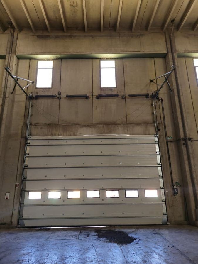 Grande porte sectionnelle blanche partiellement ouverte dans un bâtiment industriel en béton.