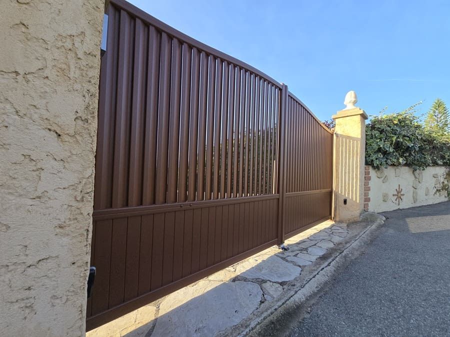 Portail en métal brun, faisant partie d'un mur, sur fond de ciel bleu clair.