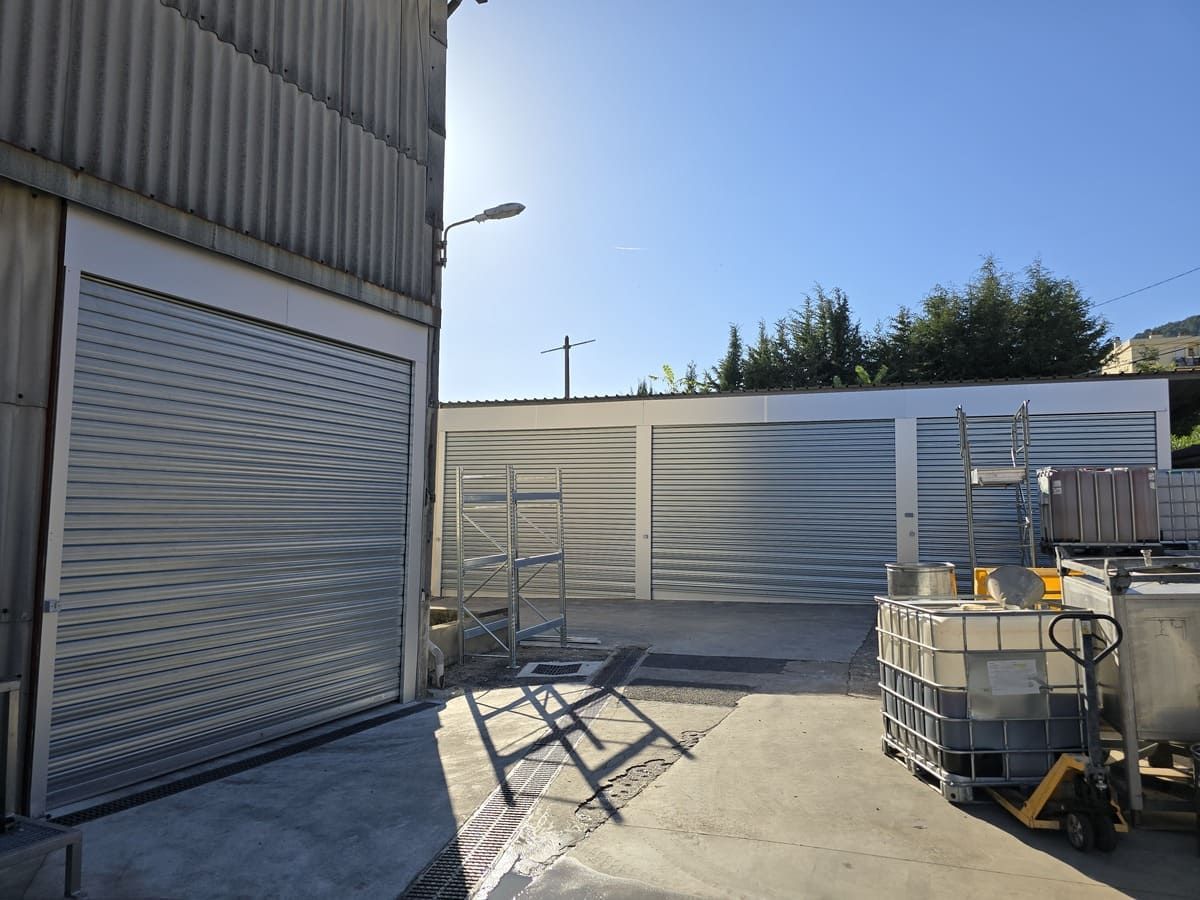 Vue extérieure d'un bâtiment industriel avec un volet métallique fermé et la lumière du soleil projetant des ombres.