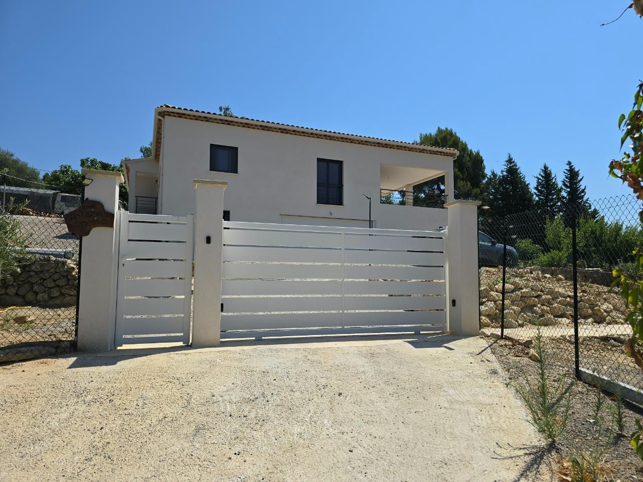 Maison blanche avec portail à claire-voie blanche ; allée de gravier. Ciel bleu.
