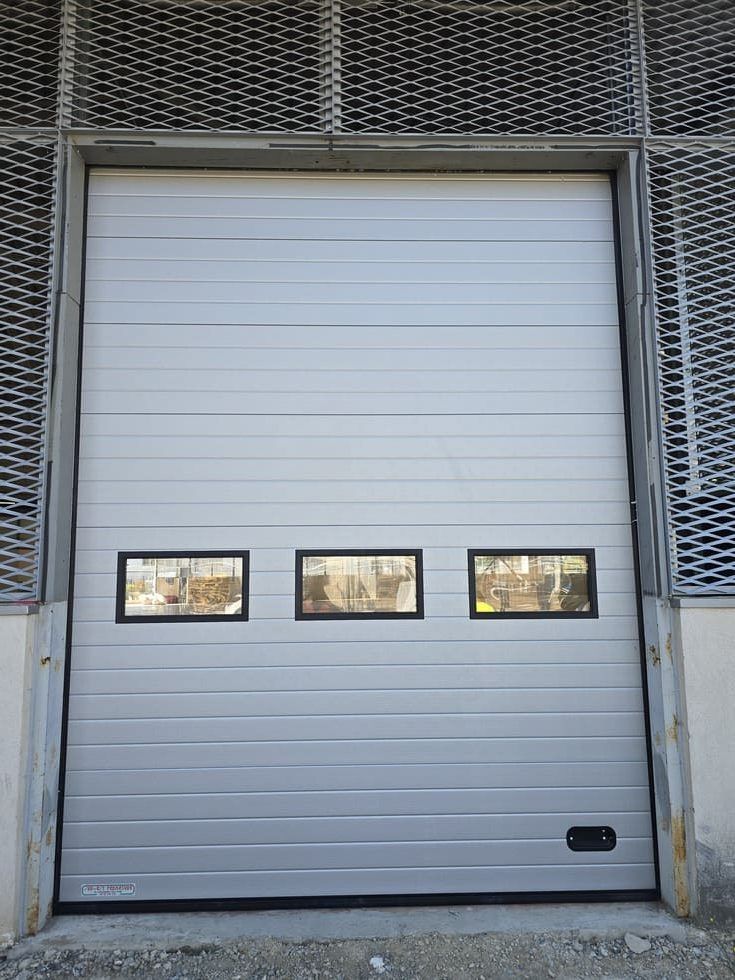 Porte sectionnelle industrielle grise avec trois fenêtres rectangulaires.